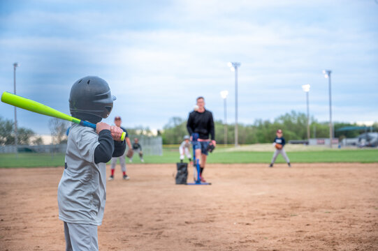 Young player practices hitting during evening baseball session at local field in spring season