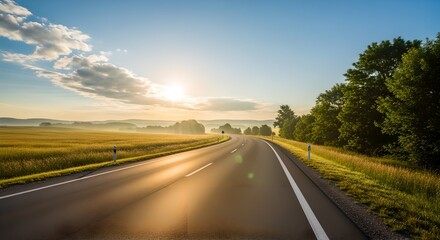 Long summer road stretching toward bright glowing sunrise in wide landscape.