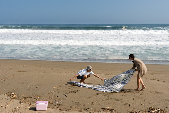 Young couple laying blanket on beach for relaxation