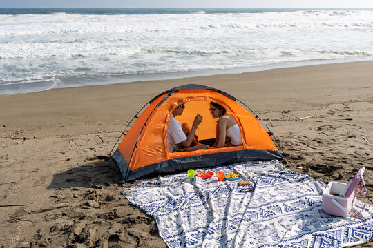 Young couple relaxing inside tent on sandy beach enjoying picnic