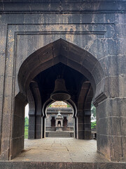Naklejka premium A serene view of an ancient temple at Wai, Maharashtra, framed through stone arches with a large bell and intricate carvings, showcasing rich Maratha-era architecture.