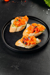 Salmon canapes on baguette with cucumber and cream cheese on black plate