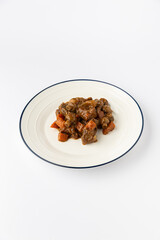 Hearty meat stew with carrots in rich brown gravy on a plate, studio isolated