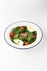 Spinach salad with tuna, cherry tomatoes and boiled egg on white background