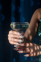 woman holding a glass of champagne, woman  in festive shiny clothes with a glass of champagne, hands on a blue fabric background, blue velvet curtains, Holiday party, corporate event, new year celebra