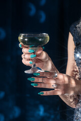 woman holding a glass of champagne, woman  in festive shiny clothes with a glass of champagne, hands on a blue fabric background, blue velvet curtains, Holiday party, corporate event, new year celebra