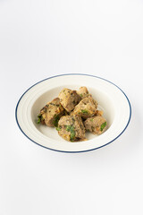 Roasted meat bites with herbs on plate, rustic home cooking, studio photo on white