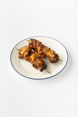 Grilled chicken skewers on a white plate, studio shot of kebab shashlik ready to serve