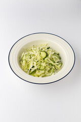 Fresh cabbage and cucumber salad with dill in a bowl on white background