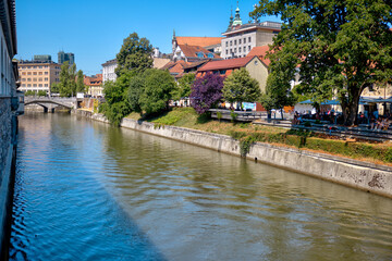 Obraz premium Ljubljana, Slovenia – July 14, 2025: A scenic view of the Ljubljanica River as it winds through the historic center of Ljubljana. Lined with trees, cafés, and charming riverside architecture. 