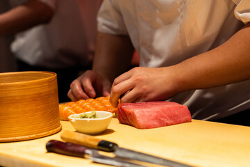 Sushi chef preparing fresh fish and sushi rolls on wooden countertop