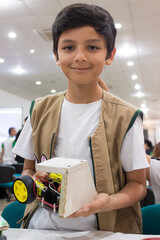 Portrait of a Hispanic boy smiling and looking at the camera with a robot in his hands inside an auditorium in Neiva, Huila, Colombia. Concept of science and robotics