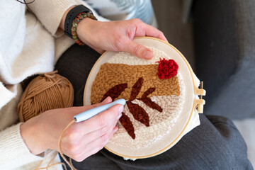 A person skillfully creates an embroidery piece with a yarn in a cozy indoor setting, showcasing dedication to crafting during a relaxing afternoon.