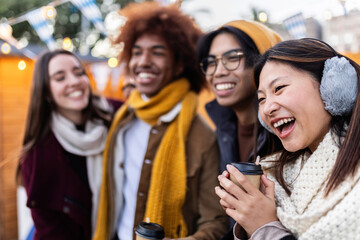 Group of young people having fun together during wintertime at a christmas market, drinking hot beverages and laughing