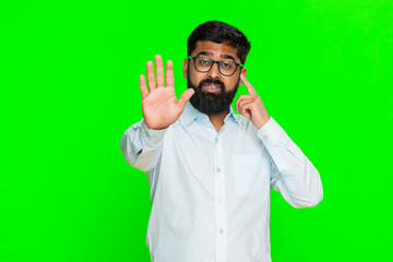 Indian man raises hand in front showing stop gesture with serious look, expressing warning and demand to be heard. Arabian guy isolated on green chroma key background asking for attention and silence.