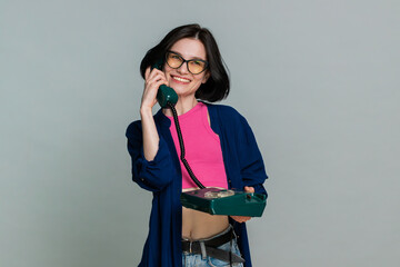 Young woman emotionally speaks into a retro wired telephone actively explaining something, expressive reaction gestures. Girl demonstrates engaging conversation and emotion isolated on gray background