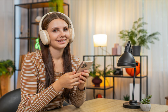 Young woman at home listens to work podcast in headphones writes ideas to notes on smartphone with focus. Caucasian girl at desk plans tasks for week sets goals saves tips and keeps calm learning pace