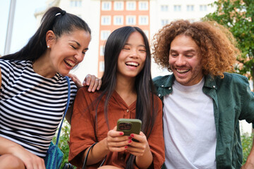 Three happy students are watching funny videos and laughing together while sitting outdoors