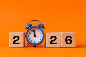 The year 2026. Wooden blocks with the date and a stylish alarm clock. Beautiful orange background. Close up. Happy New Year