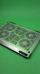 A sleek, modern computer cooling pad with multiple fans and a perforated surface designed for efficient heat dissipation, placed on a vibrant green background