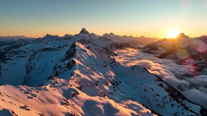 Aerial panoramic view of snow-covered mountains illuminated by sunrise, with clouds filling the valleys below. Stunning natural landscape capturing the golden light of dawn, ideal for adventure, trave - Powered by Adobe