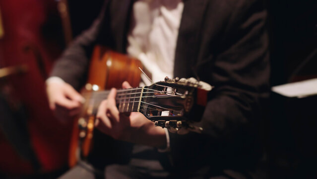 Concert view of acoustic electric guitar player with vocalist and rock band performing in a club, male musician guitarist on stage with audience in a crowded concert club hall arena, hands on guitar
