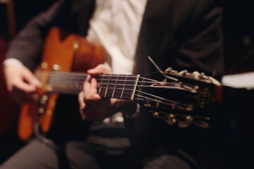 Fototapeta premium Concert view of acoustic electric guitar player with vocalist and rock band performing in a club, male musician guitarist on stage with audience in a crowded concert club hall arena, hands on guitar