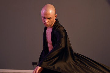 A man dressed in a flowing black robe captures movement in a striking black and white photograph,...