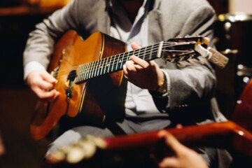 Fototapeta premium Concert view of acoustic electric guitar player with vocalist and rock band performing in a club, male musician guitarist on stage with audience in a crowded concert club hall arena, hands on guitar