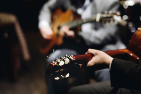 Concert view of acoustic electric guitar player with vocalist and rock band performing in a club, male musician guitarist on stage with audience in a crowded concert club hall arena, hands on guitar