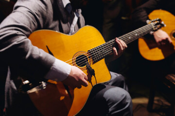 Obraz premium Concert view of acoustic electric guitar player with vocalist and rock band performing in a club, male musician guitarist on stage with audience in a crowded concert club hall arena, hands on guitar