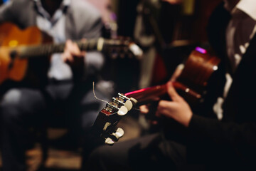 Concert view of acoustic electric guitar player with vocalist and rock band performing in a club, male musician guitarist on stage with audience in a crowded concert club hall arena, hands on guitar
