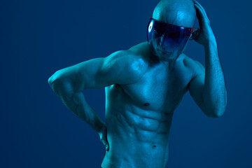Athletic man posing confidently with a stylish pair of sunglasses, showcasing strong physique and a dynamic blue background, emphasizing the mood of strength and determination.