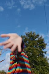 Child reaching hand toward camera in colorful striped sweater outdoors, playful motion and shallow focus against blue sky and trees, closeup perspective capturing joyful candid childhood moment.