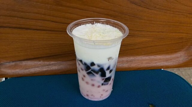 Creamy es teler served in a plastic takeaway cup, a rich Indonesian iced dessert drink made with avocado, young coconut, jackfruit, and sweet creamy mix. Street food.