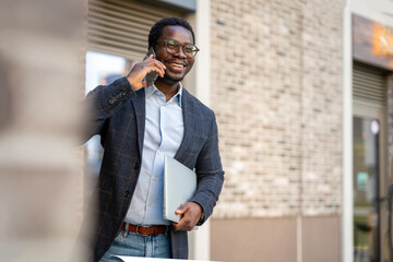 Happy black businessman talking on cell phone with laptop