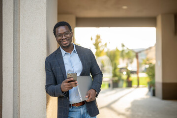Smiling black man using smartphone and laptop outdoors