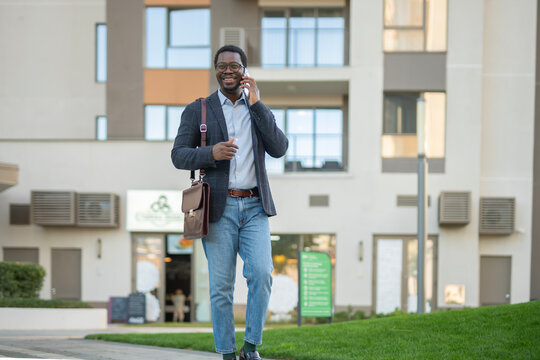 Happy black businessman talking on smartphone walking urban street - Powered by Adobe