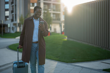 African american man checking phone while traveling with luggage