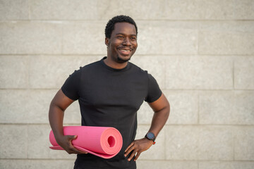 Happy black man holding yoga mat posing outdoors