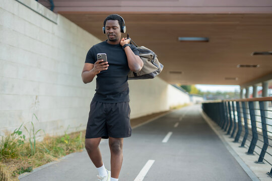 African american man walking, checking smartphone listening music