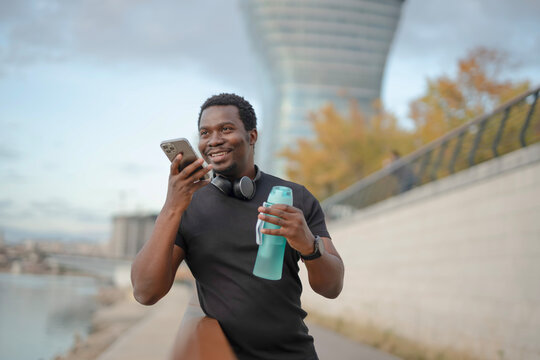 Young black man using voice assistant holding water bottle