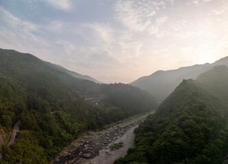 A stunning aerial view of a lush, green valley with a winding river and towering mountains under a cloudy sky at sunrise.