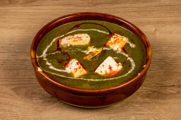 A bowl of Indian saag paneer, spinach and cheese isolated on a wooden table