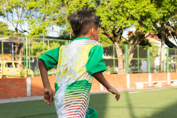 A boy Latino soccer player in a green uniform training on an synthetic grass in Neiva, Huila, Colombia. Concept of childhood and sports