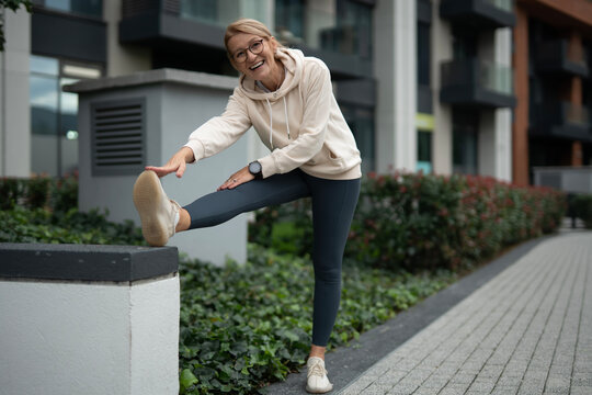 Mature woman stretching leg outdoors for fitness workout - Powered by Adobe