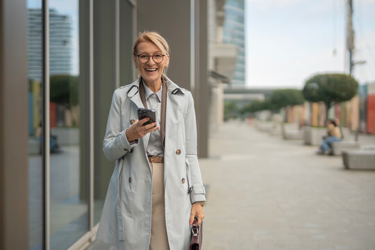 Mature business woman smiling, using smartphone outdoors