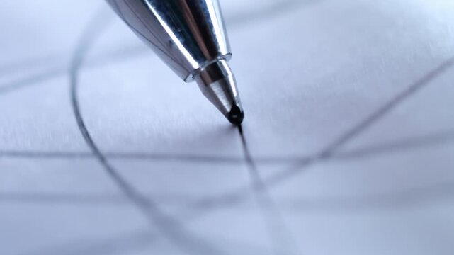 A close-up, low-angle shot of a silver ballpoint pen tip touching down on white paper ruled with a grid.