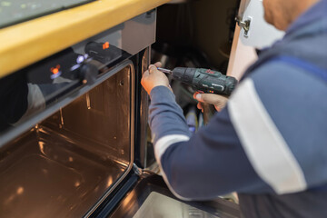 Technician installing new kitchen oven using cordless drill