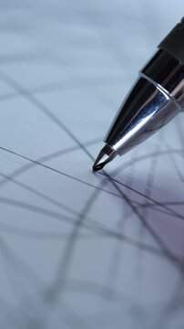 A vertical, extreme close-up of a metallic pen tip drawing intricate, chaotic lines on a piece of white paper.